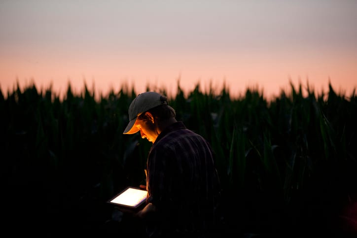 Farmer in a field at dusk, illuminated by a glowing tablet.
