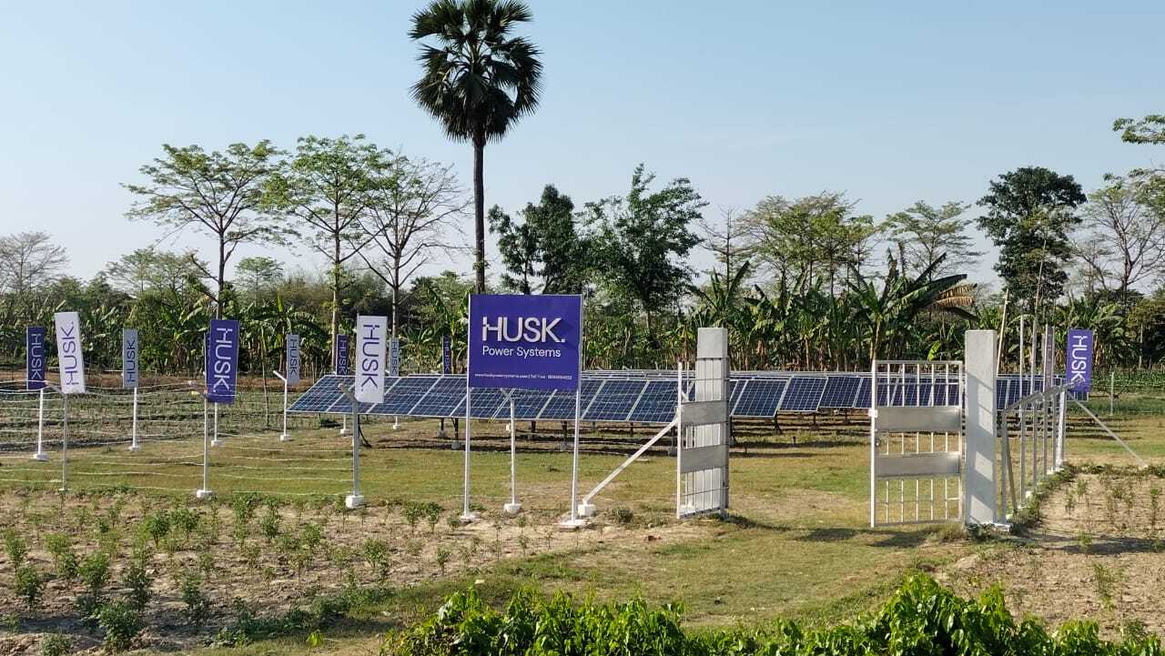 Husk Power Systems solar microgrid in a rural area with panels and signs.