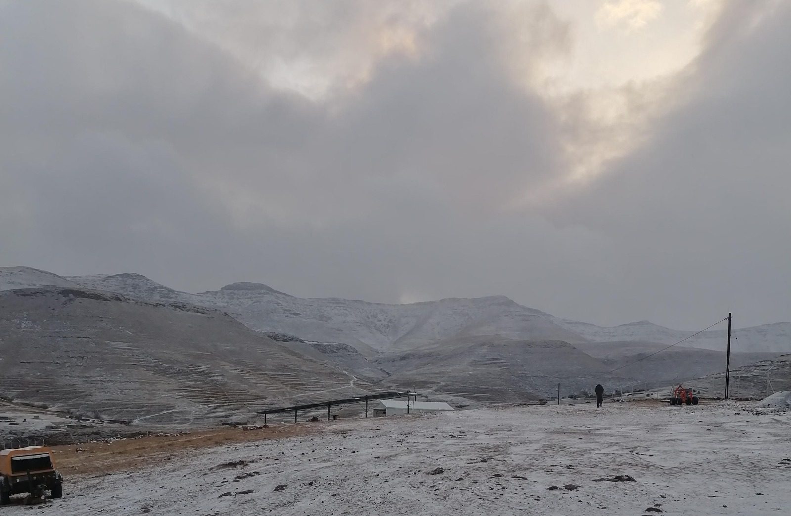 Snowy mountains, cloudy sky, building, solar panels, person, vehicles.