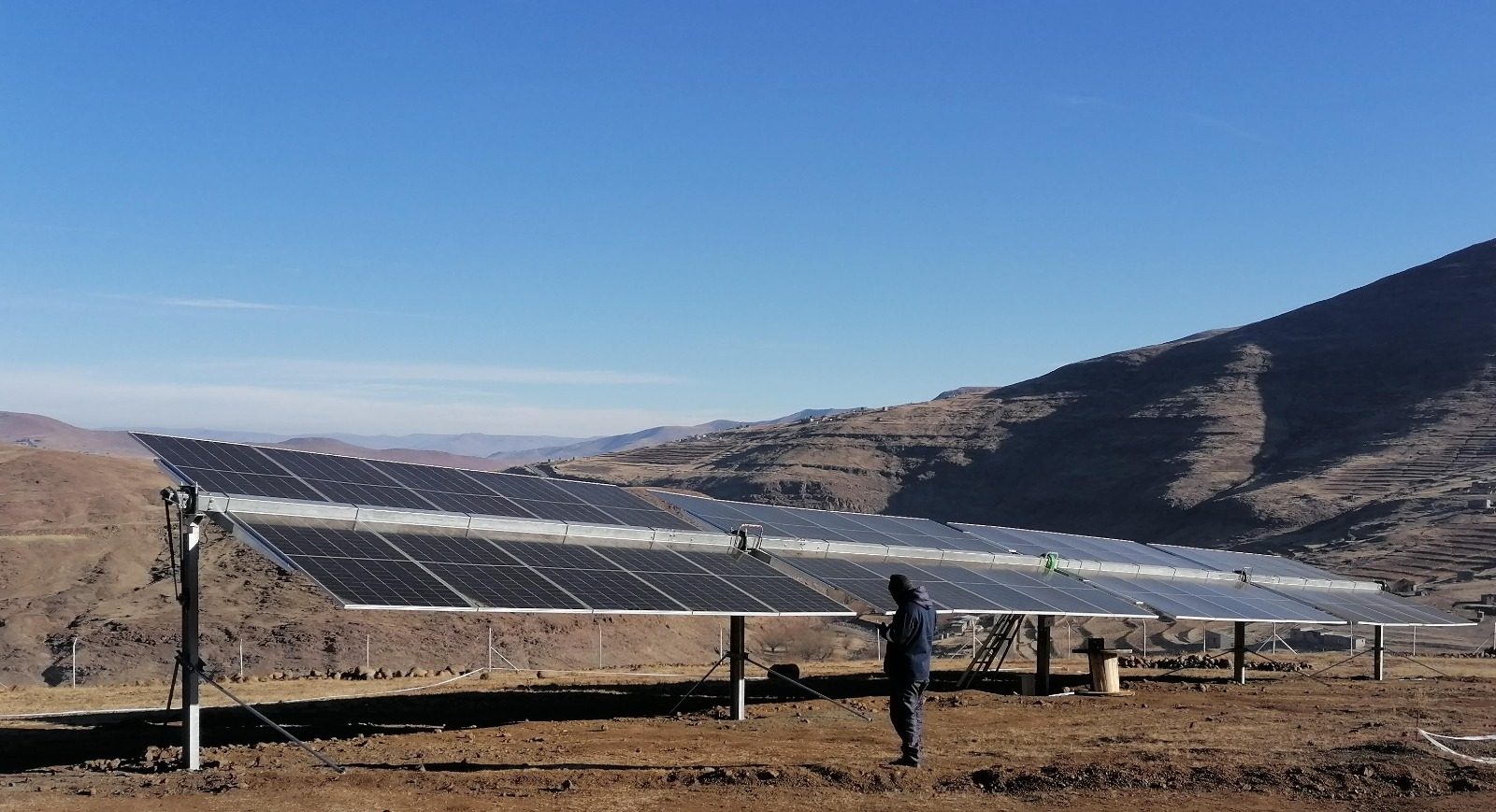 Large solar array and person in a sunny, dry, mountainous landscape.
