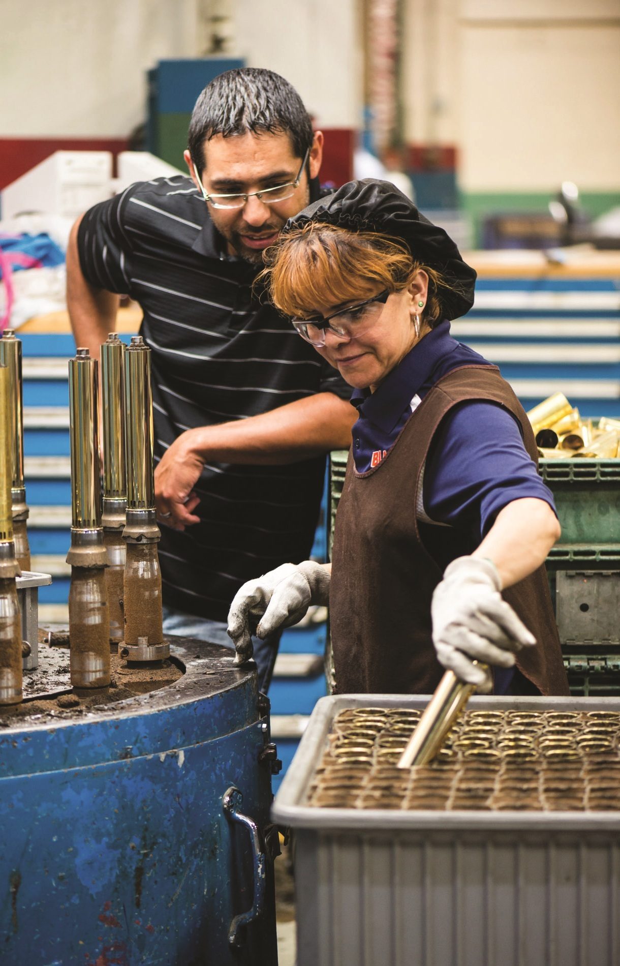 Two factory workers, a man and a woman, inspecting metal parts on an assembly line.