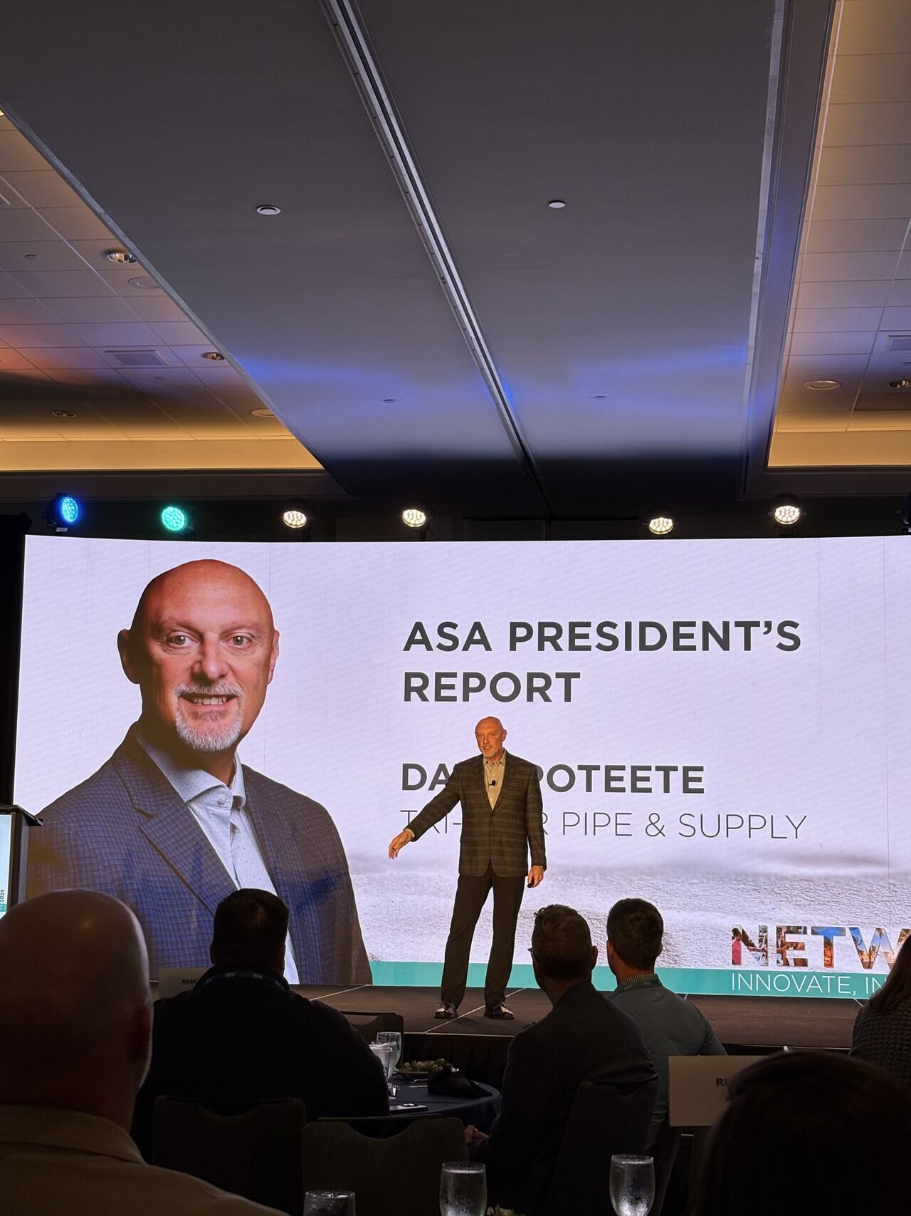 Speaker on stage with "ASA PRESIDENT'S REPORT" and his photo on a large screen.
