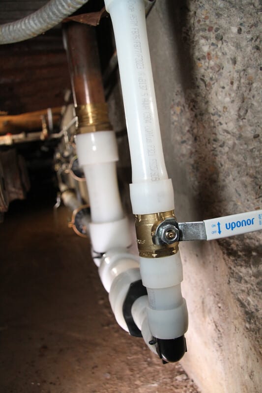 White PEX plumbing with brass fittings and an Uponor valve, connected to an older copper pipe.