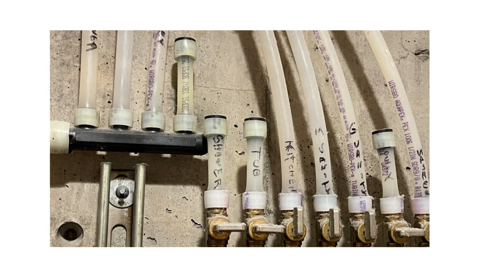 A close-up of a PEX plumbing manifold system with multiple labeled pipes for shower, tub, and kitchen.