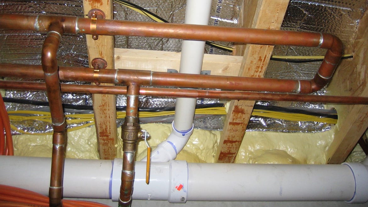 Copper and PVC pipes, wood framing, insulation, and electrical wires in a utility space.