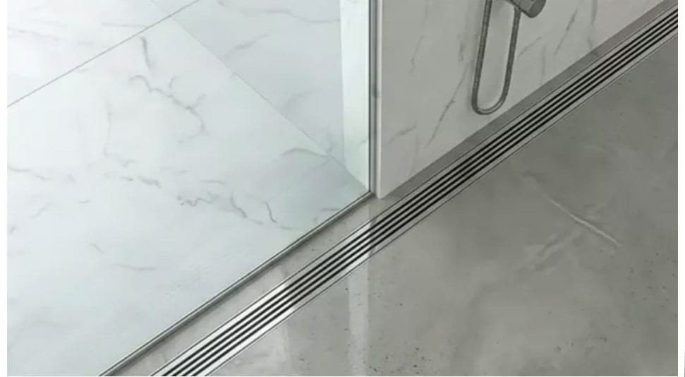 Modern shower with linear drain separating white marble and grey concrete floors, glass partition, and shower head.