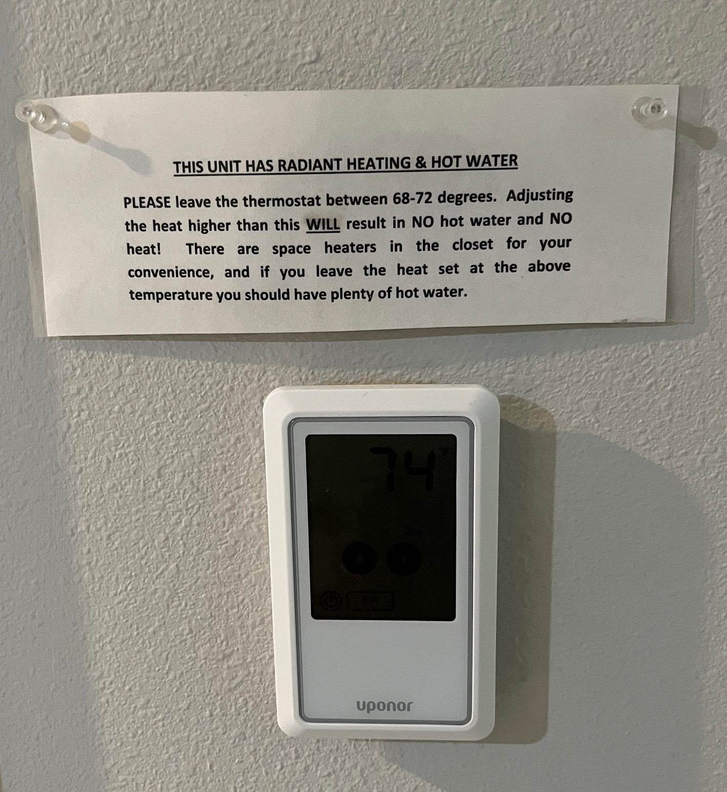 A white sign detailing radiant heating instructions above a white Uponor digital thermostat.