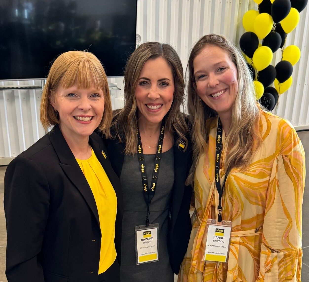 Three smiling women, including Viega's Chief People Officer and CFO, at an event.