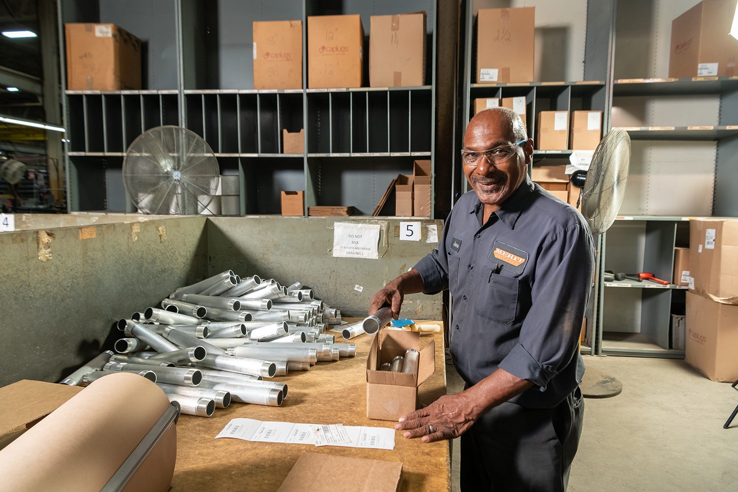 Smiling factory worker packing metal pipes into a box.