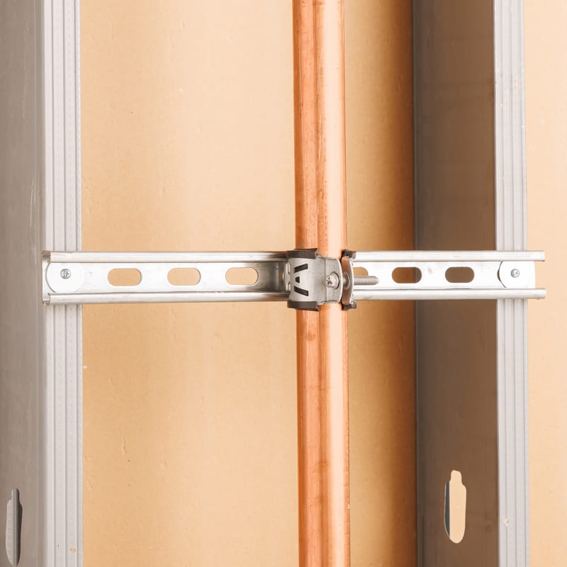 Copper pipe clamped to a metal strut channel between two metal wall studs.