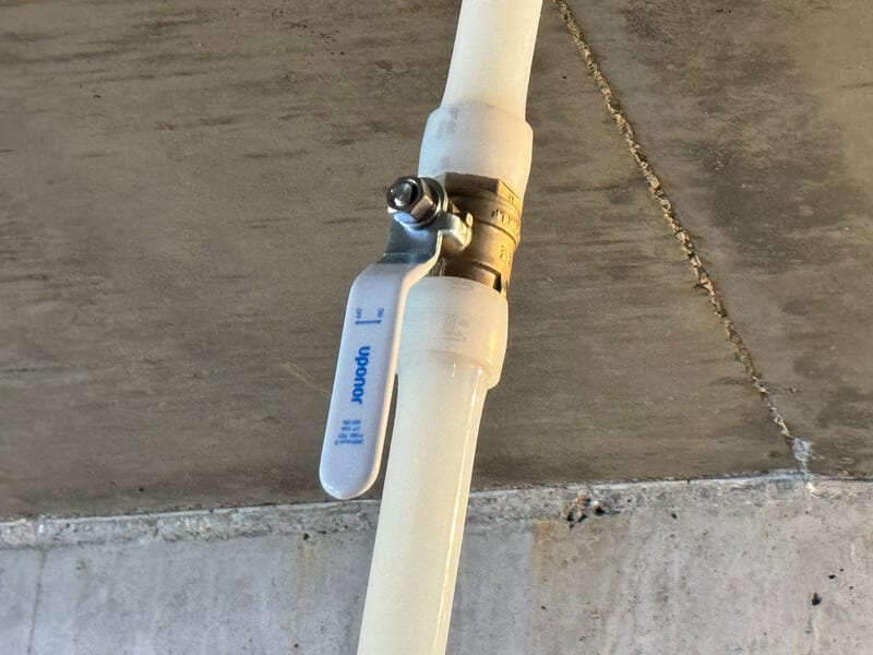 Close-up of an Uponor PEX plumbing ball valve and pipe against a concrete background.