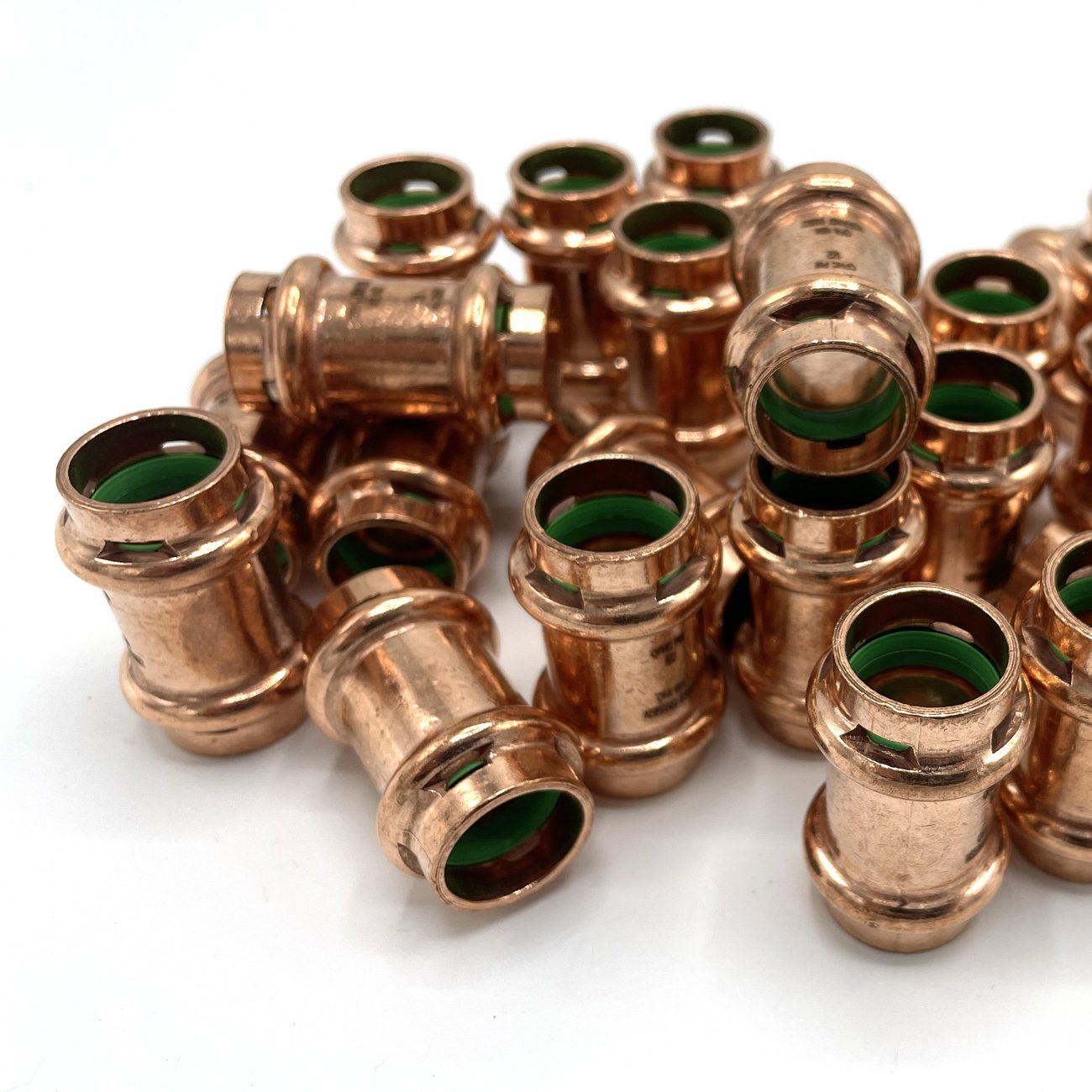 Pile of copper press fittings with green O-rings on a white background.