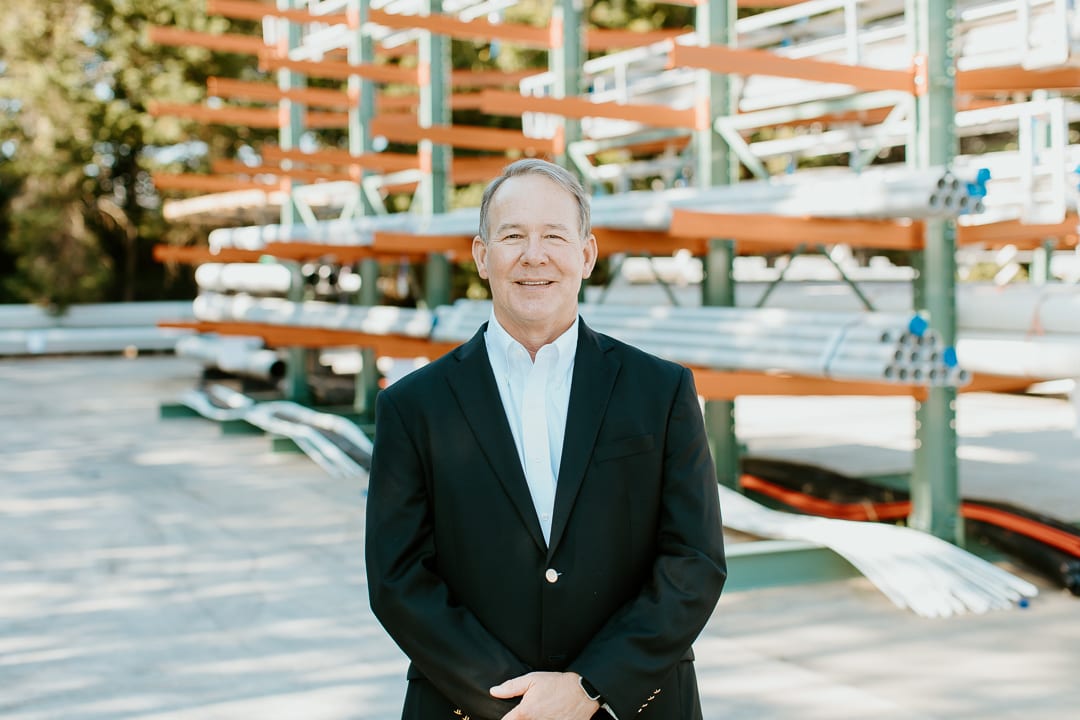 Smiling man in suit in front of pipe storage racks.