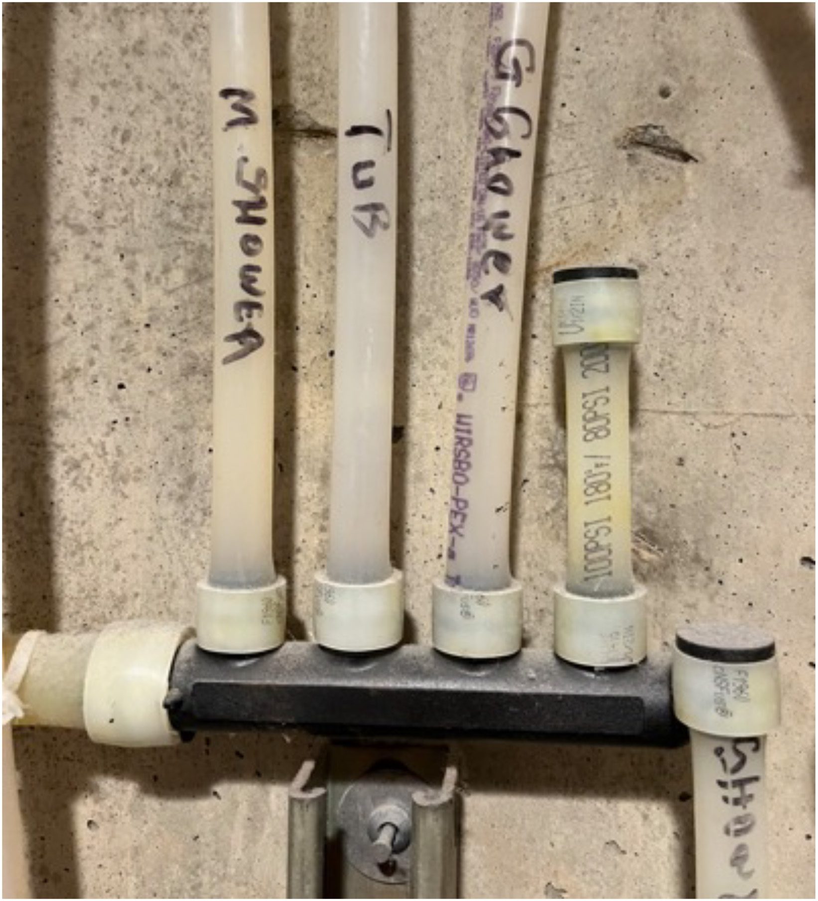 Plumbing manifold with PEX pipes labeled "M Shower," "Tub," and "G Shower," connected to a main line.