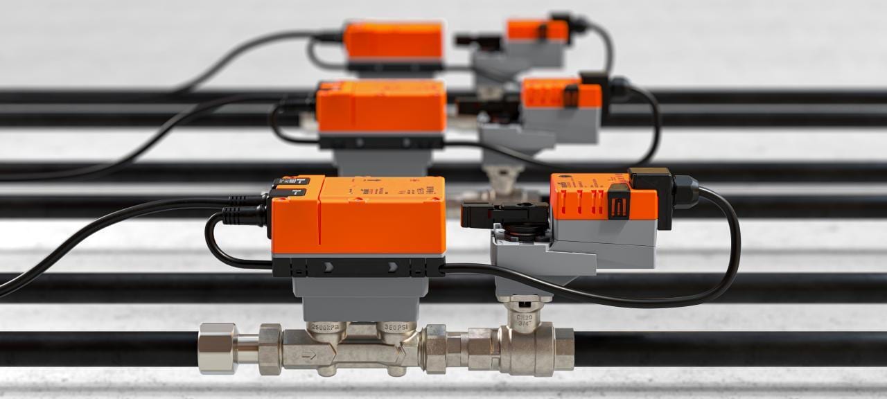 Multiple orange and grey industrial control valves with black cables installed on pipes in a row.