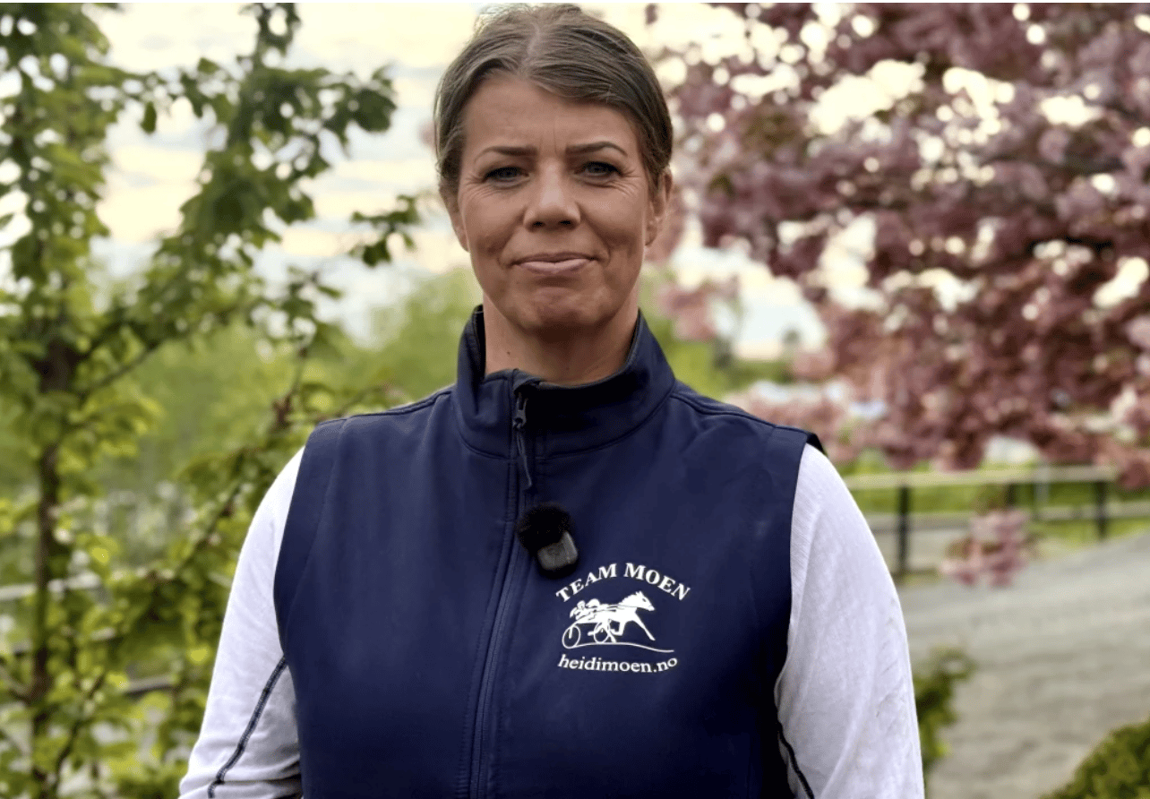 Woman in a navy vest with "TEAM MOEN heidimoen.no" logo, smiling slightly outdoors.