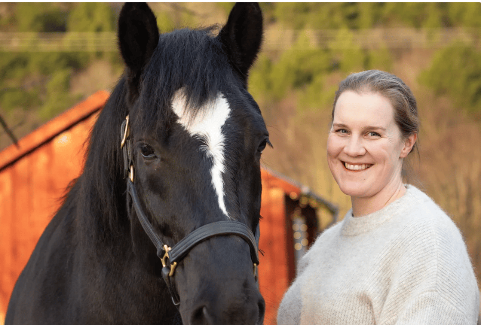 Smiling woman and black horse with white blaze.
