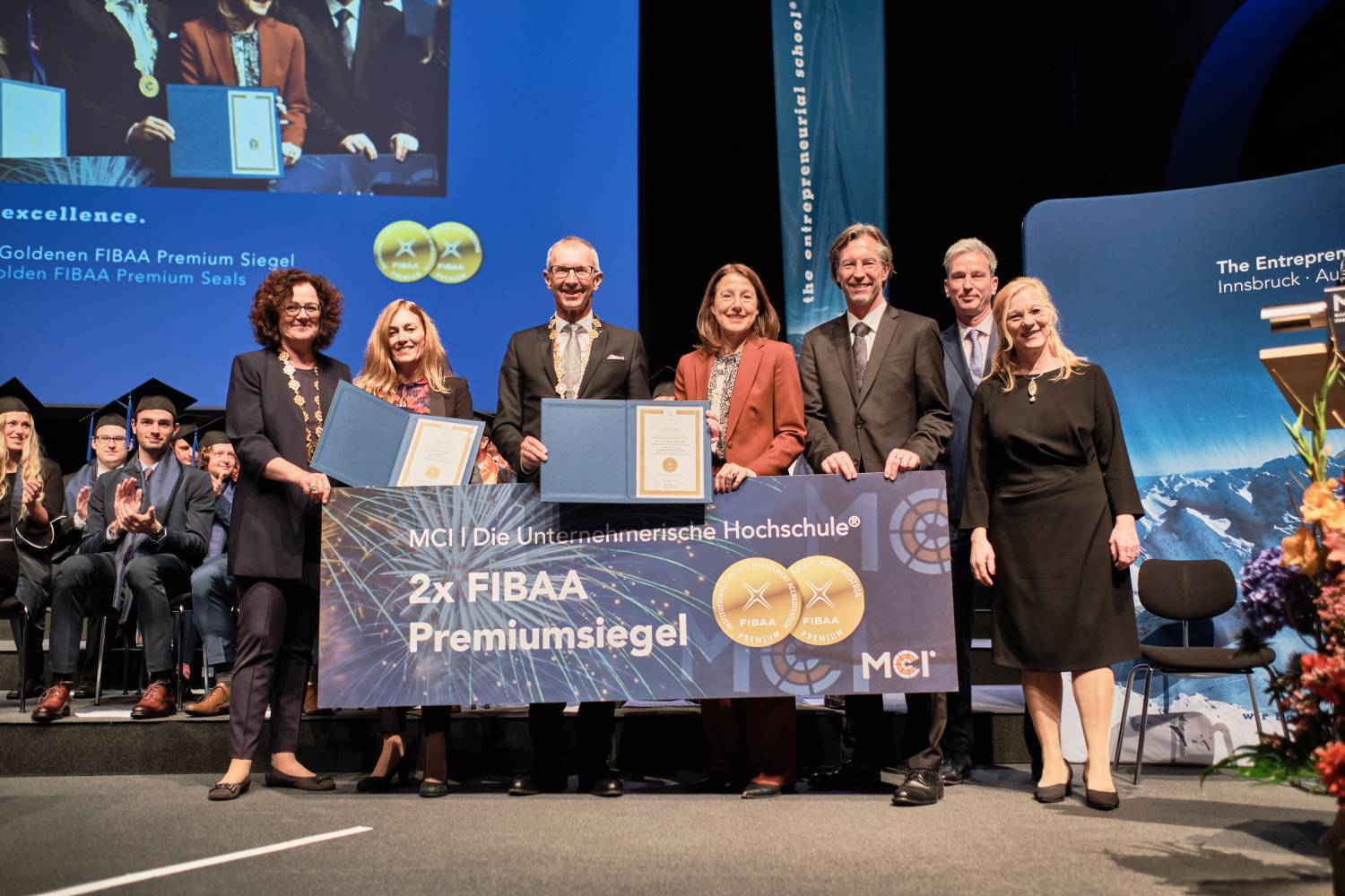 A group of people on a stage holding certificates and a banner celebrating MCI's FIBAA Premium Seals.