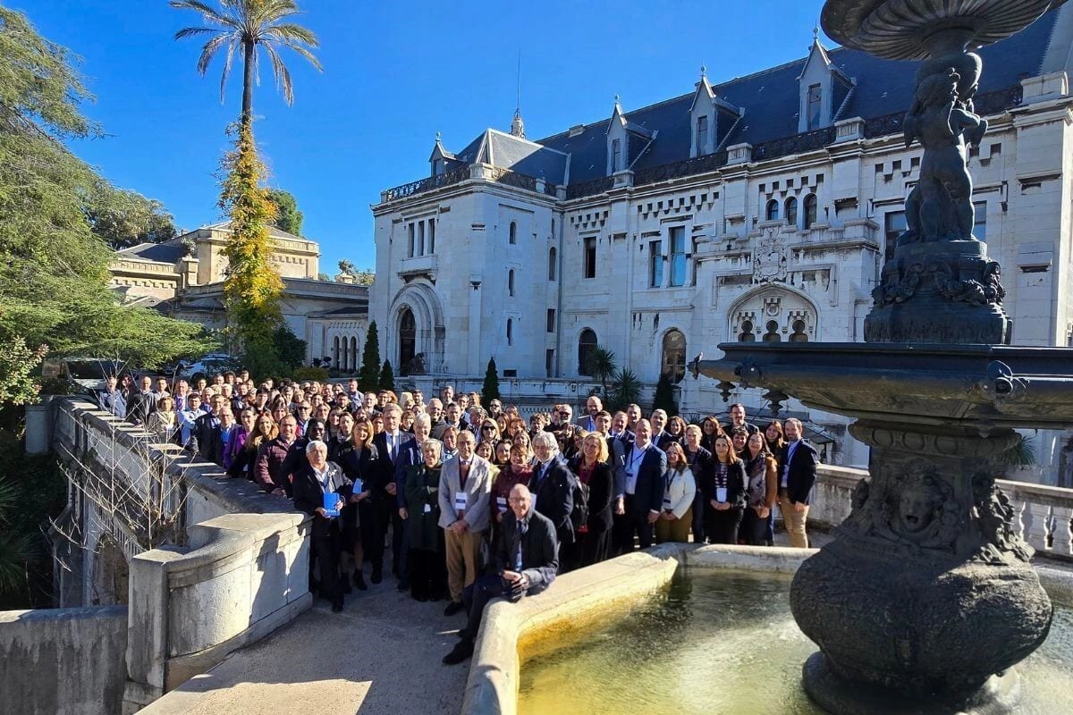 A large group of people gathered outdoors for a photo in front of a grand historic building.