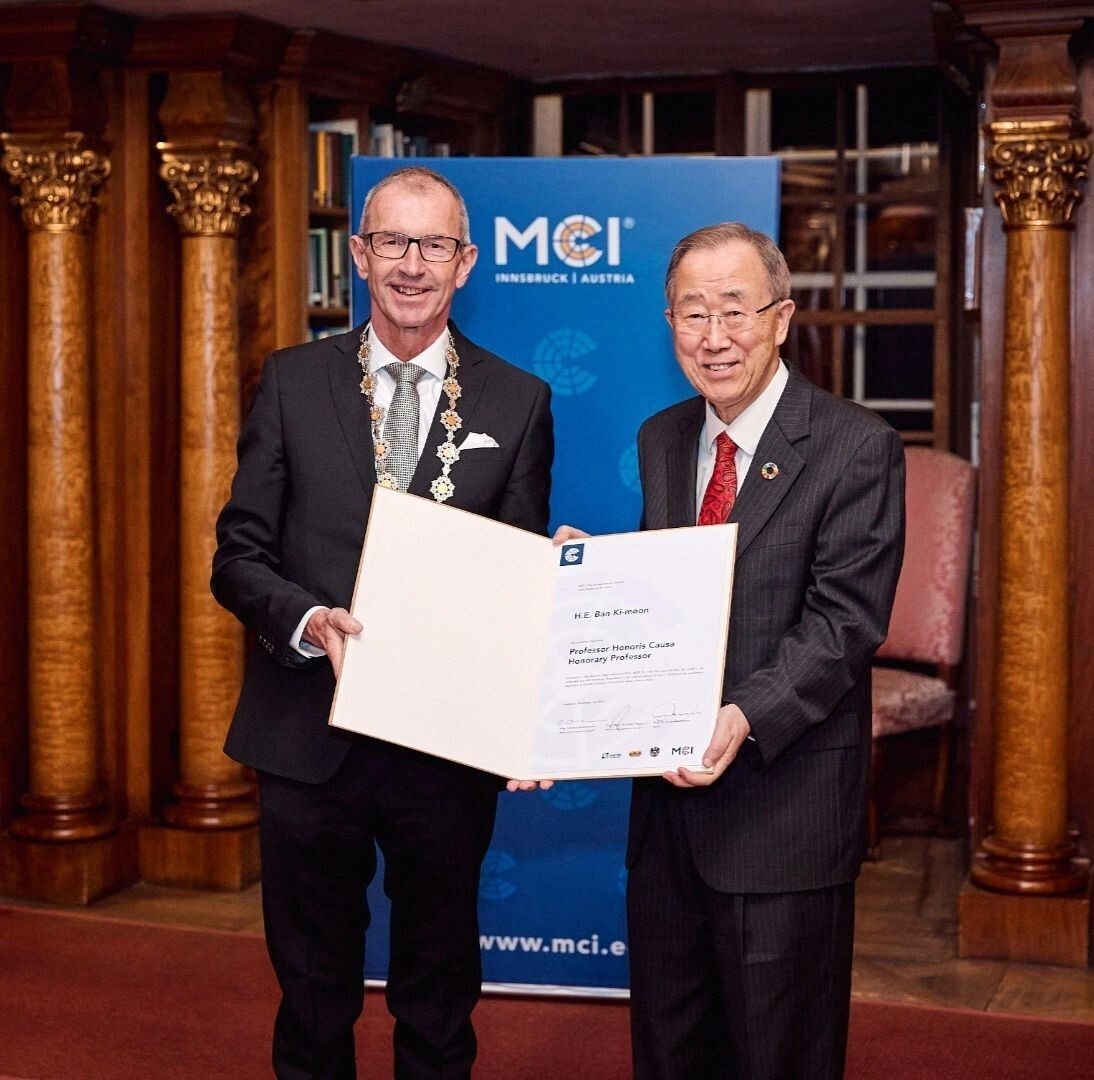 H.E. Ban Ki-moon and another man holding his Professor Honoris Causa certificate from MCI Innsbruck.