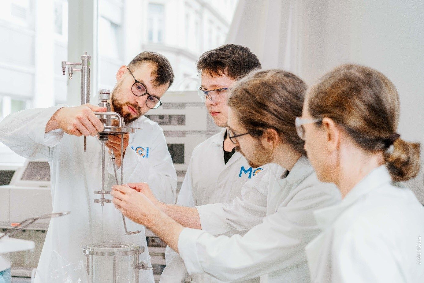 Four scientists in lab coats assembling complex laboratory equipment.