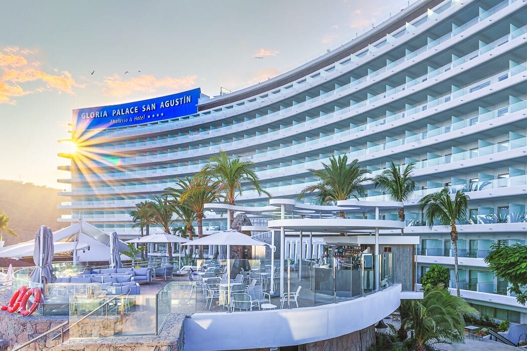 Hotel Gloria Palace San Agustín with sunburst, curved balconies, outdoor terrace, and palms.