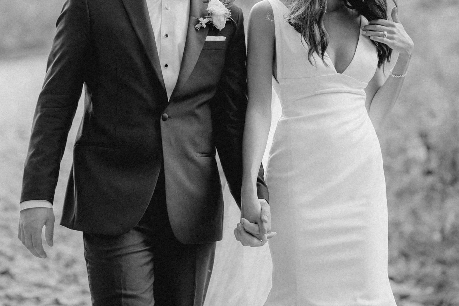 B&W photo of a wedding couple walking hand-in-hand.