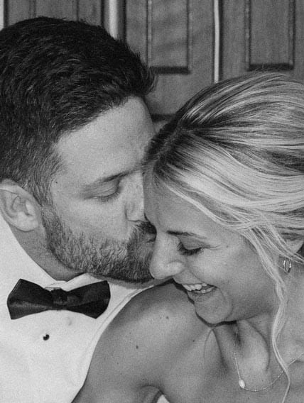A man with a beard kisses a laughing woman on the cheek in a black and white photo.