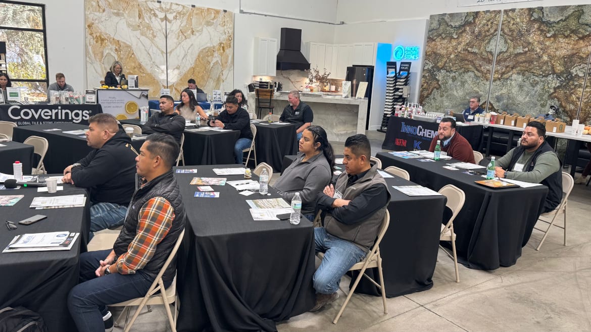 People attend a presentation in a showroom, seated at tables with stone slab walls.