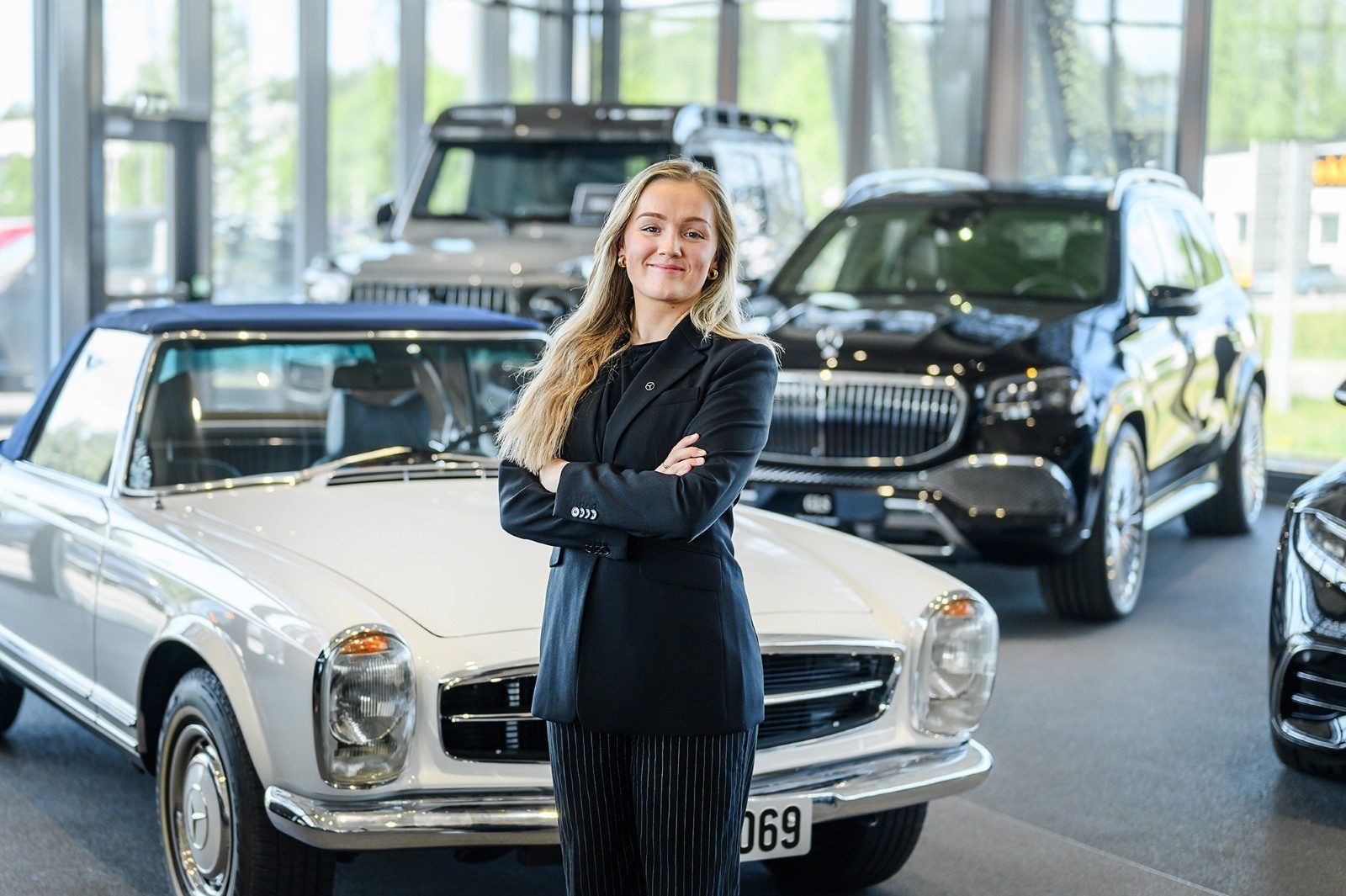 Smiling woman with crossed arms in a luxury car showroom.