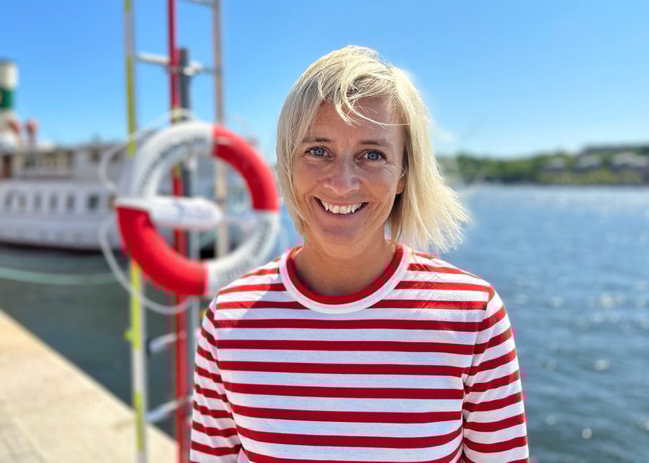 Smiling woman in red-striped shirt by water, with a lifebuoy.