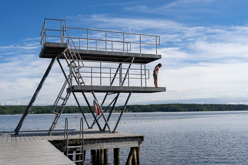 A child on a high diving platform looks down at a lake.