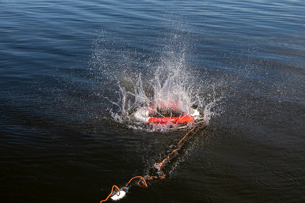 Red and white device splashing into dark water, with orange rope.