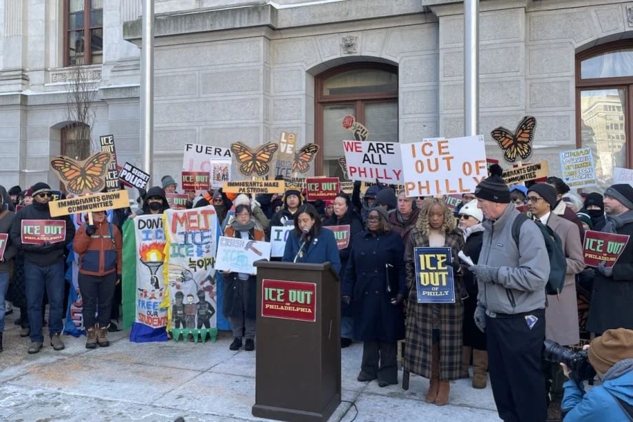 Protest against ICE outside a building; people hold "ICE OUT" and "Immigrants Grow Communities" signs.