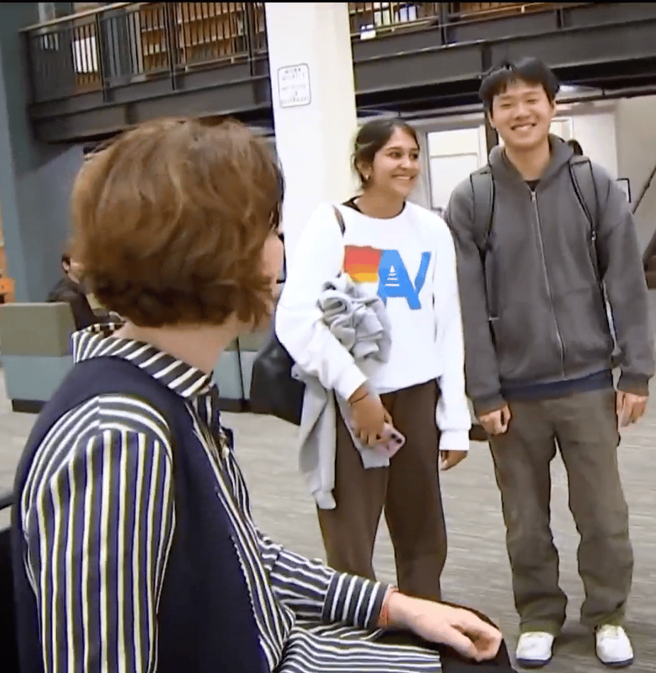Three young people, two smiling, are standing and interacting in a bright, modern interior space.