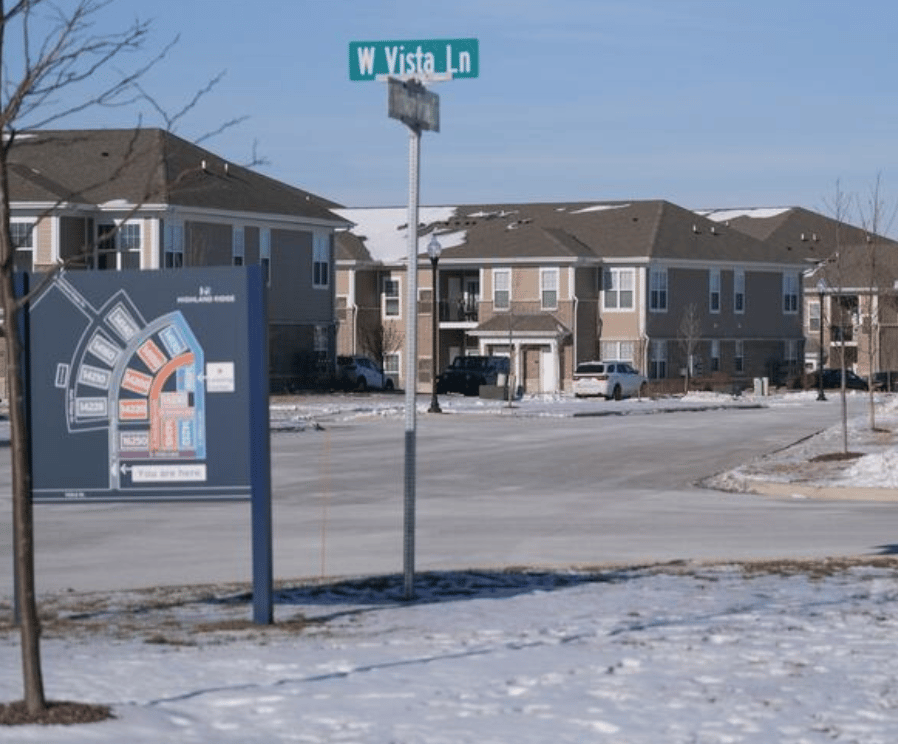 A snowy scene showing apartment buildings, a street sign for W Vista Ln, and a map of the complex.