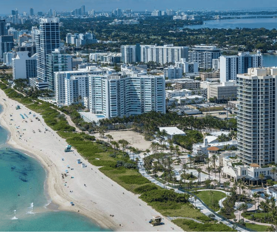 Coastal city aerial: high-rise buildings, sandy beach, and turquoise ocean.