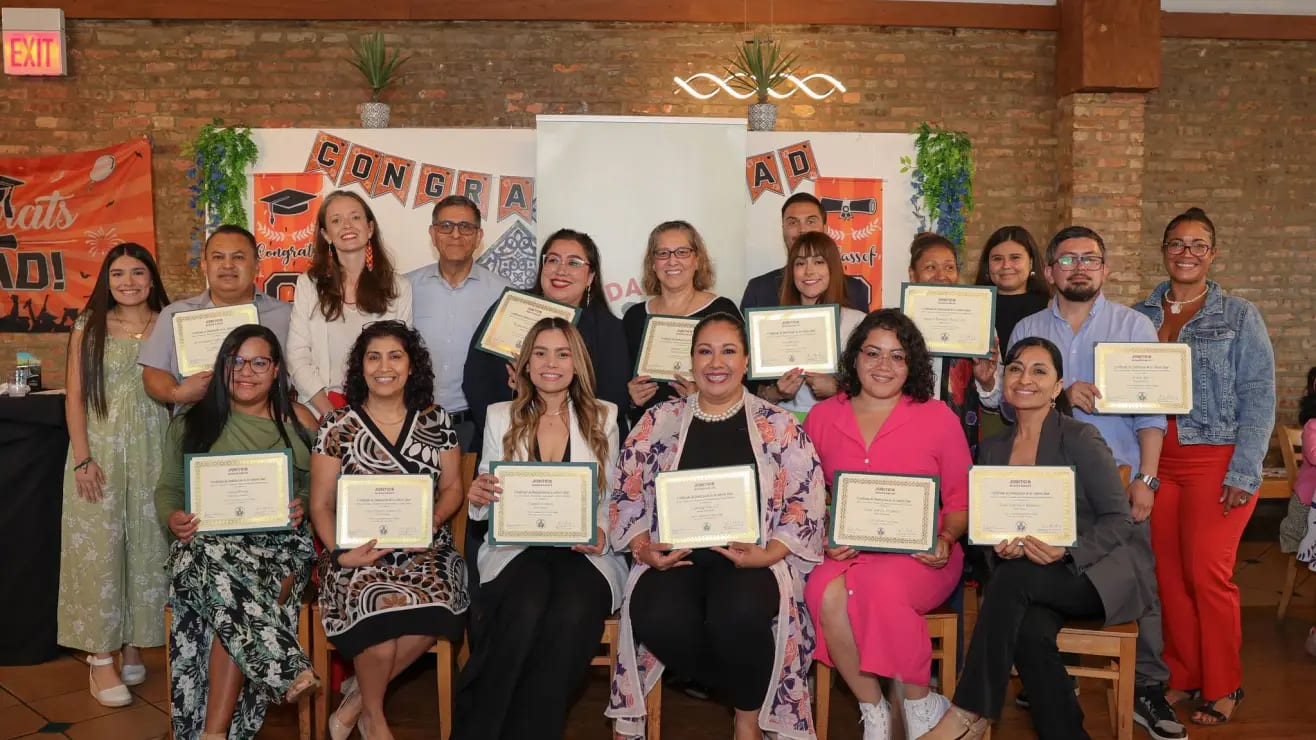 A diverse group of adults holding certificates, smiling for a photo, celebrating their graduation or achievement.