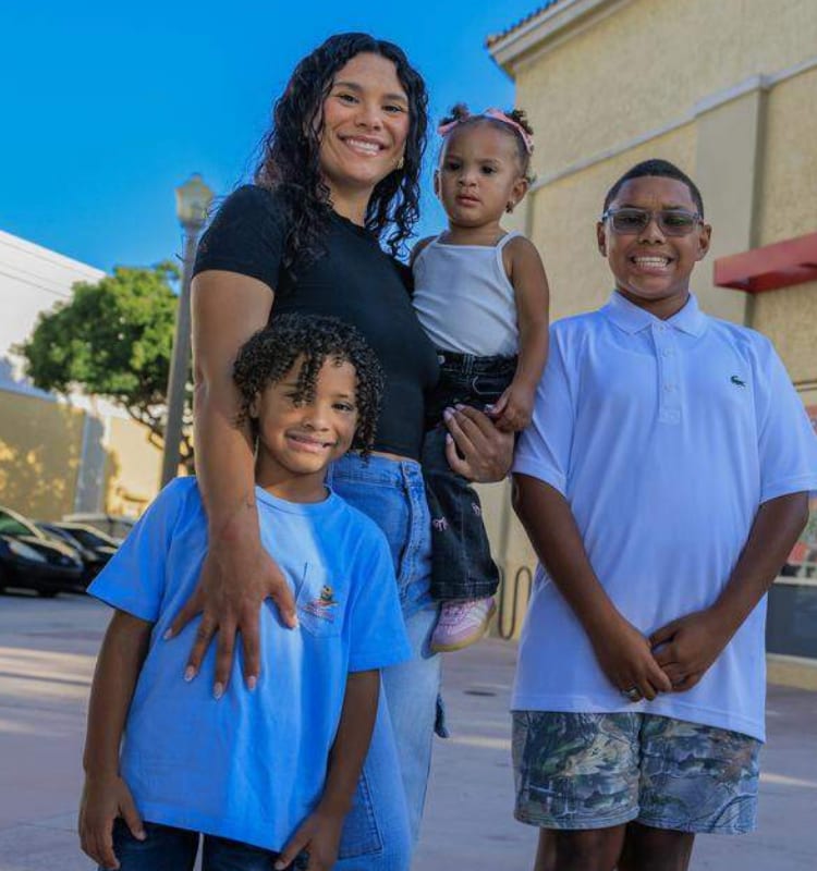 A happy family portrait of a mother smiling with her three children: a young boy, a baby girl, and an older boy.
