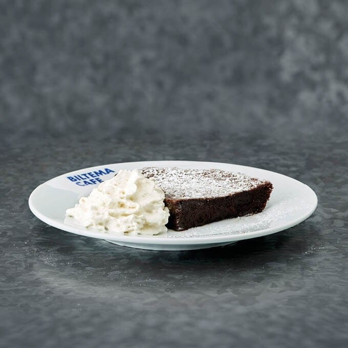 Chocolate cake with whipped cream on a Biltema Cafe plate, dusted with powdered sugar.
