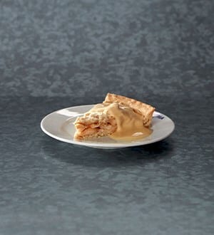 Slice of apple pie with caramel sauce on a white plate.