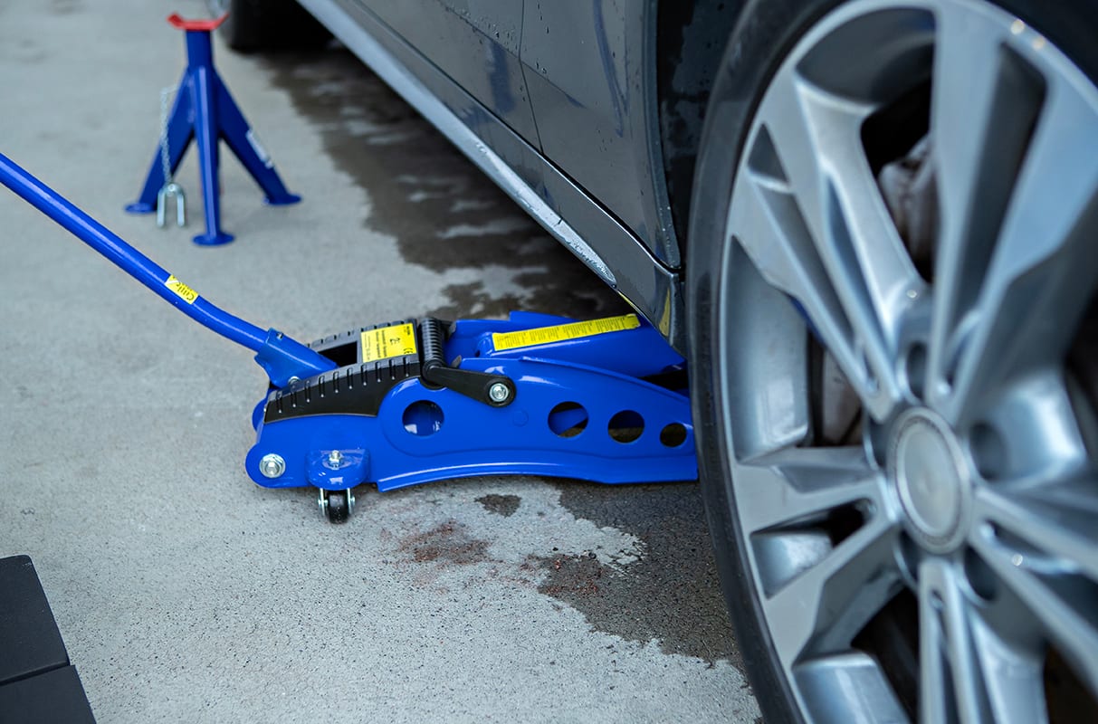 Blue car jack lifting a black car, with a blue jack stand nearby.