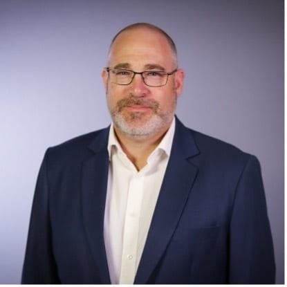 Headshot of a man with glasses and beard in a blue suit.