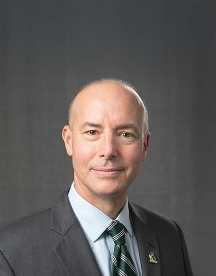 Smiling bald man in a gray suit and green striped tie.