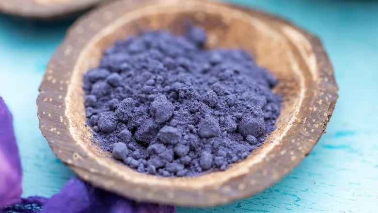 Vibrant blue butterfly pea flower powder in a rustic wooden bowl.