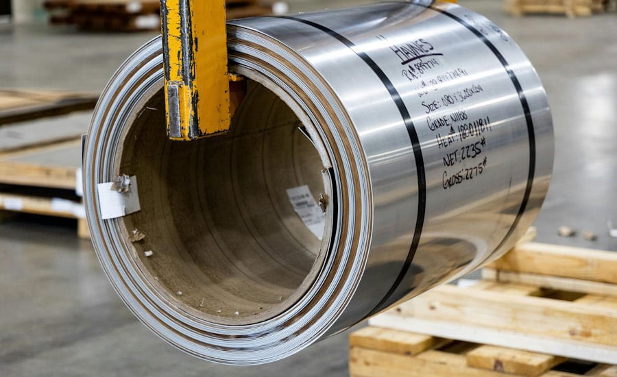 Large metal coil with text, hanging from lifting equipment.