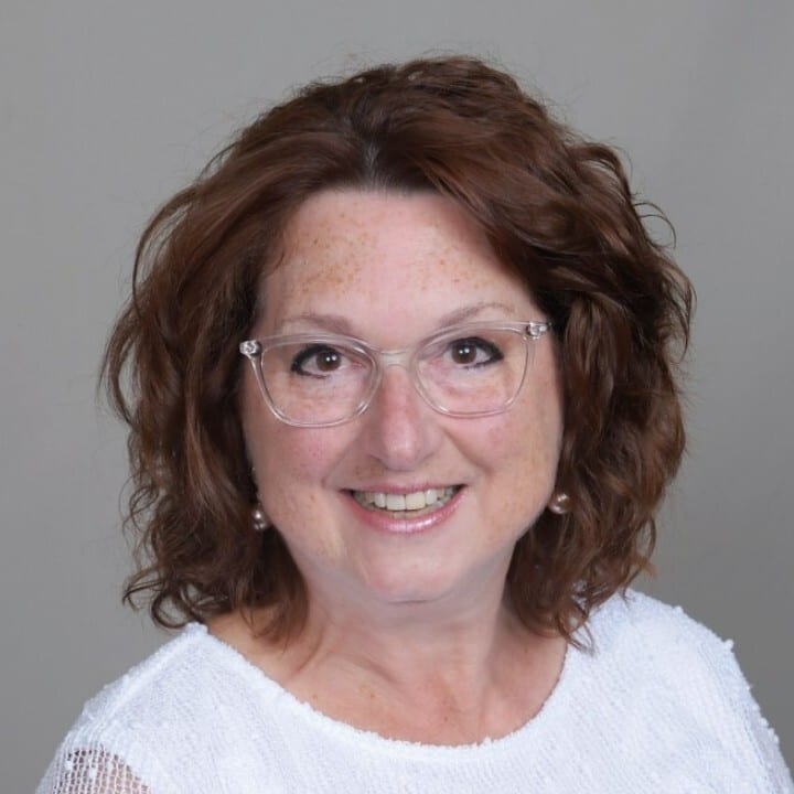 Headshot of a smiling woman with glasses, curly red hair, and freckles.