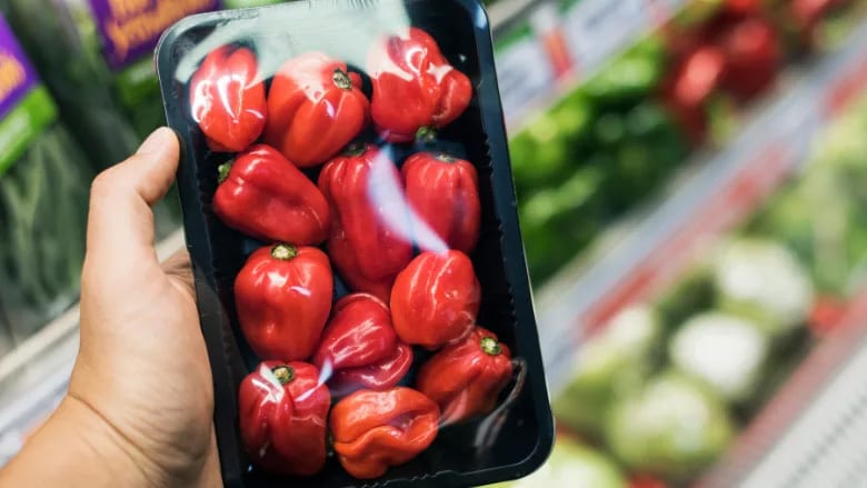 Hand holding a plastic tray of red bell peppers in a supermarket.