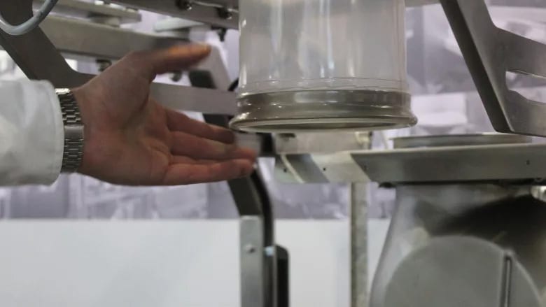 A person's hand in a lab coat and watch near a clear container on industrial equipment.