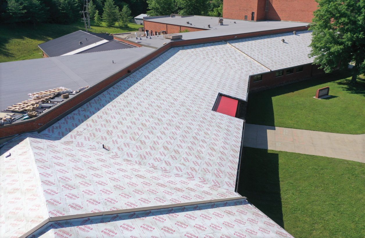 Aerial view of a building roof under renovation, covered with white 'ULTRA HT' underlayment and a red skylight.